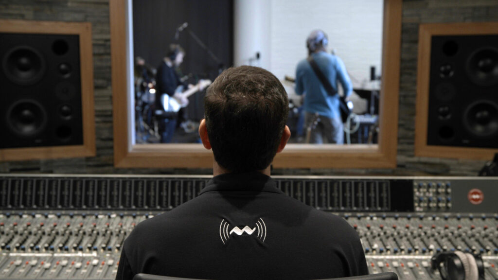 Engineer mixes at the console while a rock band performs in the Live room.